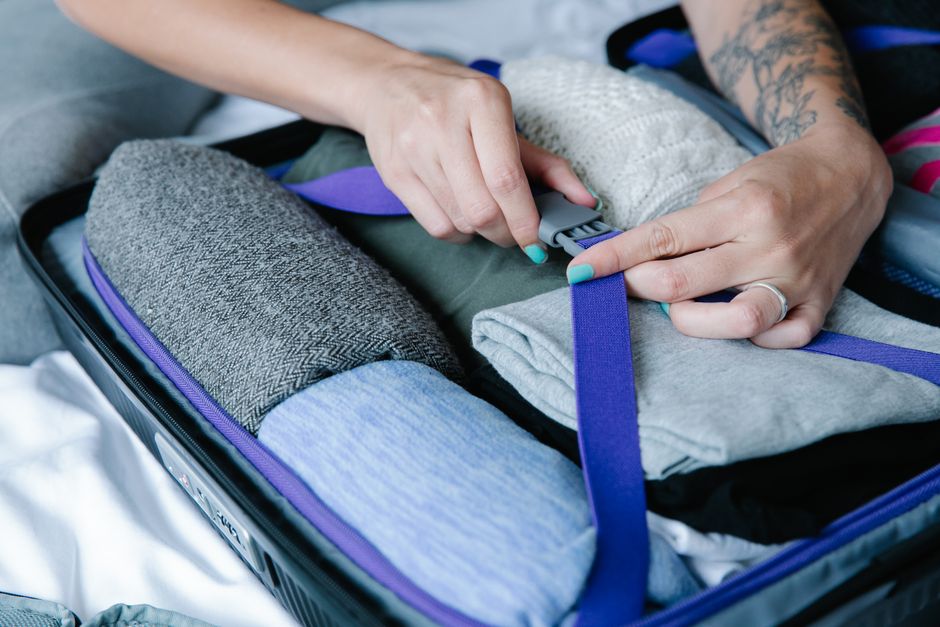 Person packing a suitcase efficiently, strapping folded clothes inside.