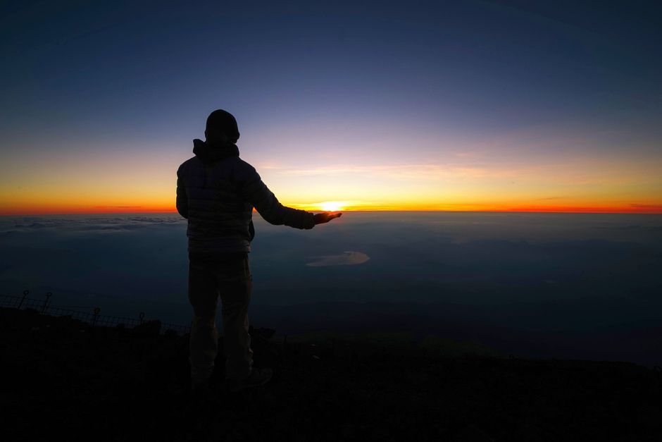 A hiker stands against the stunning sunrise from Mount Fuji, Japan, capturing tranquility and adventure.
