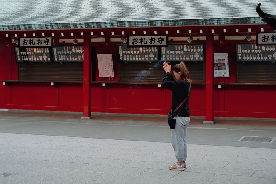 A woman prays at a traditional Japanese temple, with hanging charms in the background.